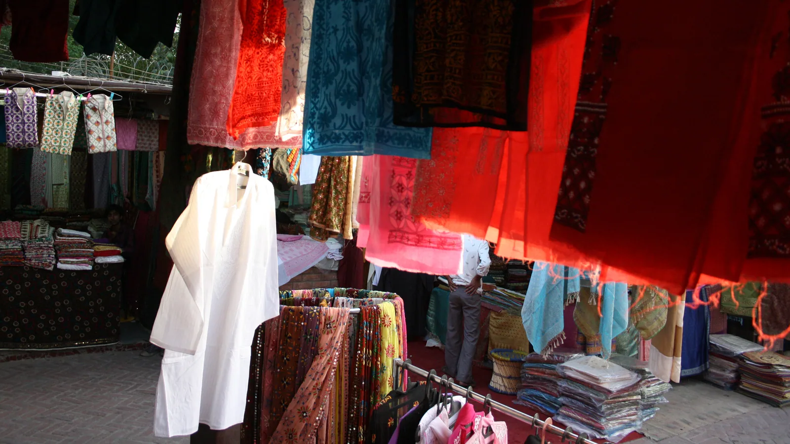 A row of colourful men's kurtas hanging on wooden hangers inside a traditional Mumbai shop