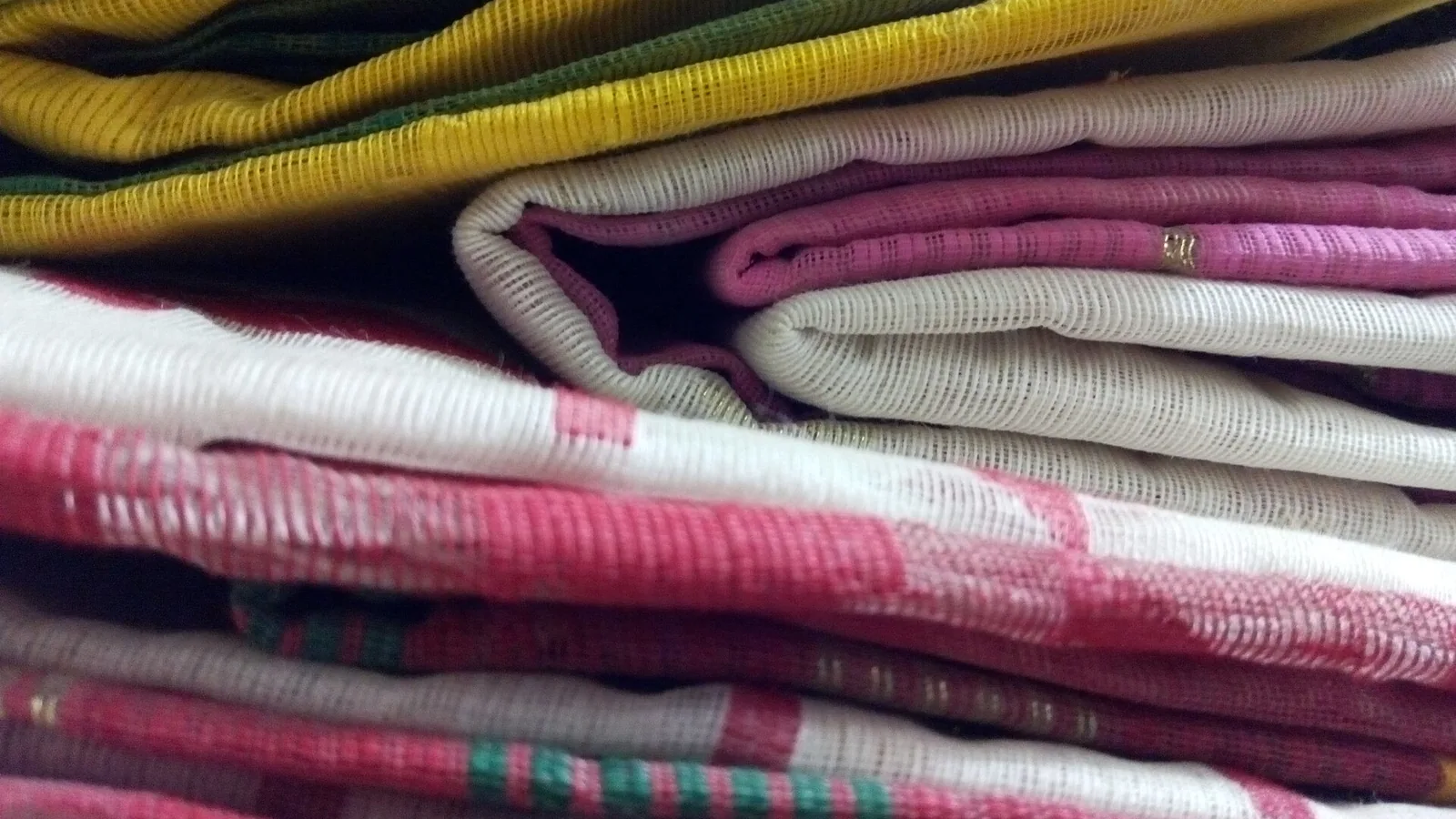 A shop owner using a smartphone to photograph a folded saree on a white sheet near a window